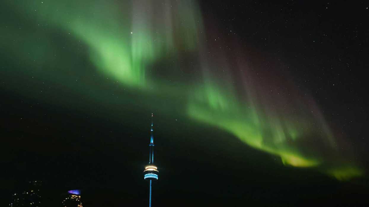 green northern lights in night sky above cn tower in toronto