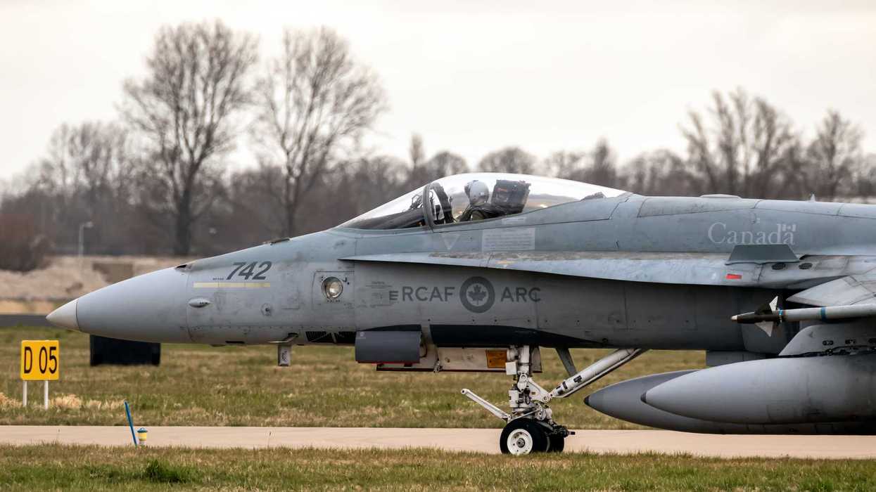 Grey RCAF-branded fighter jet taxis on the runway at an air force base.