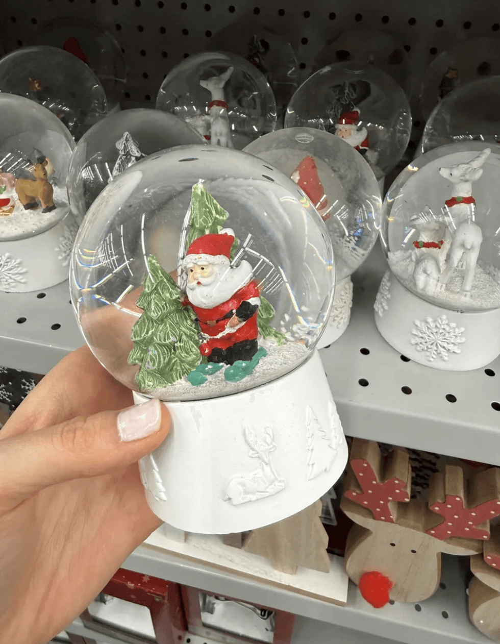 Hand holding a Santa snow globe, surrounded by similar globes on a store shelf.