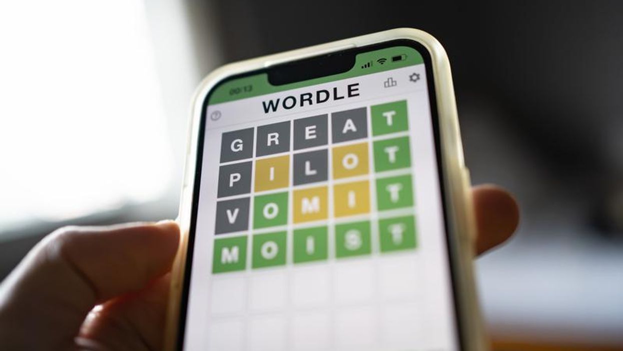 Hand holding phone with Wordle game on the screen.