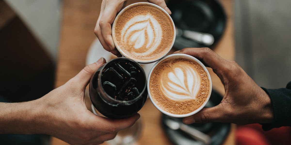 Hands holding three cups of coffee together.