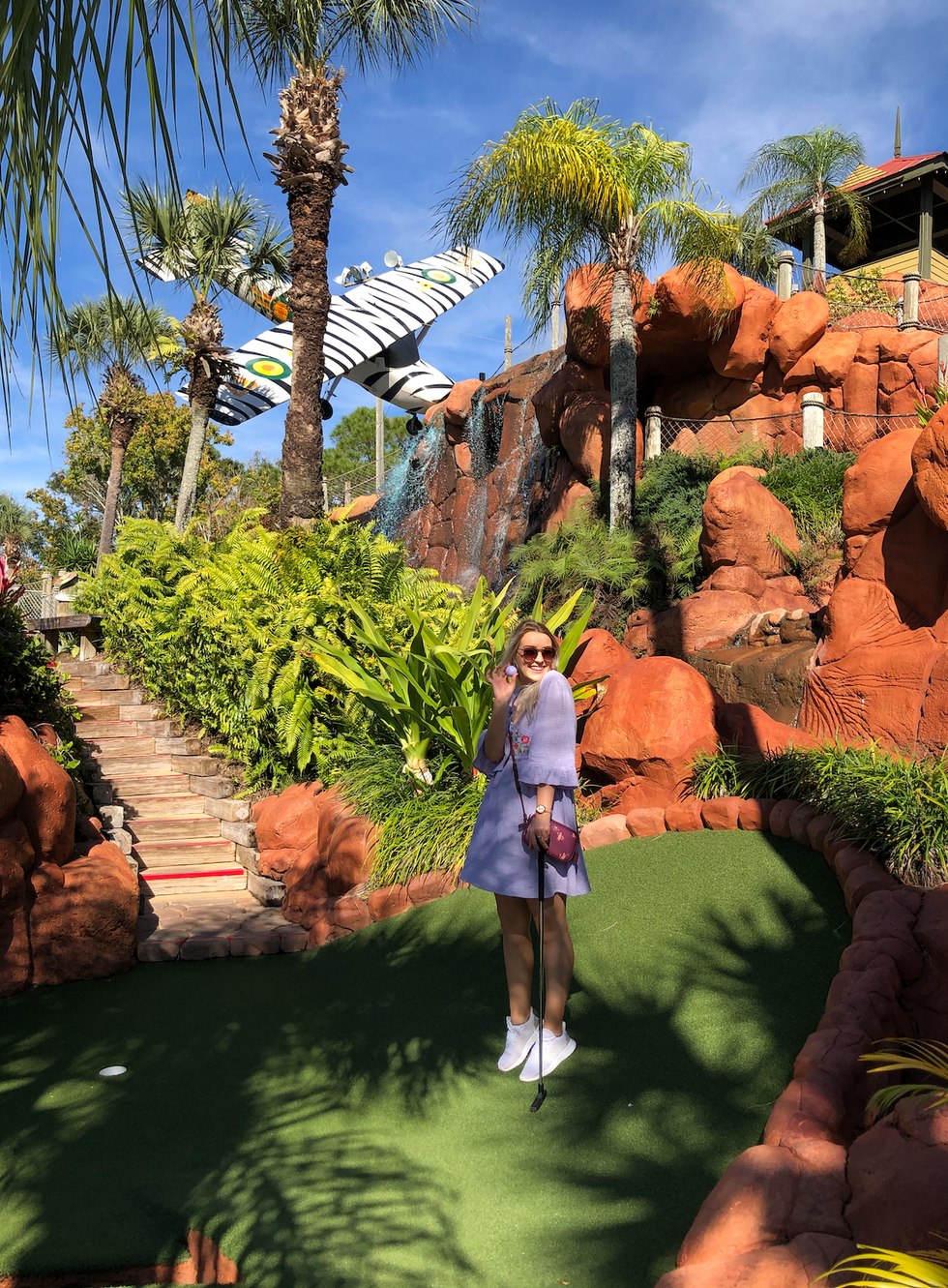 Helena holds a golf ball and smiles at a mini gold course.