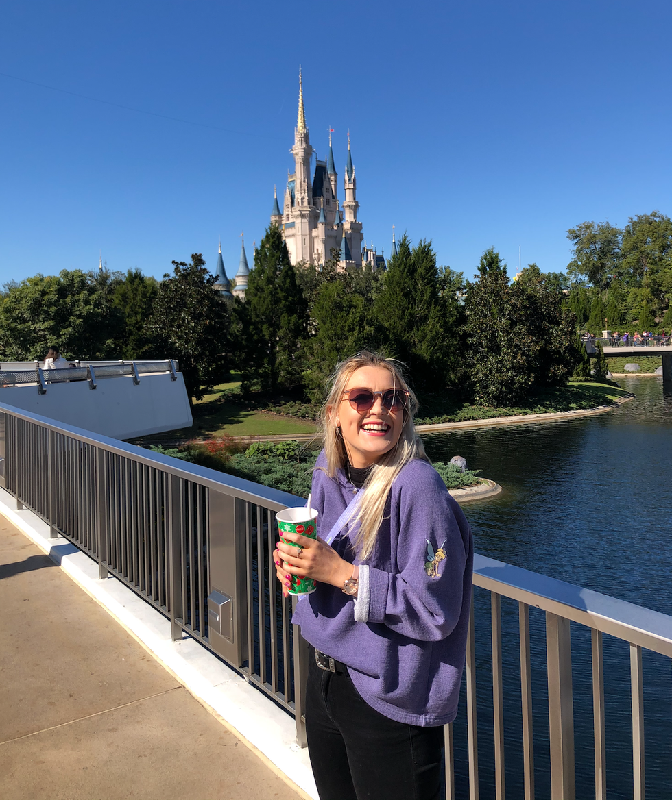 Helena smiles and poses with a drink beside the castle in Disney World.
