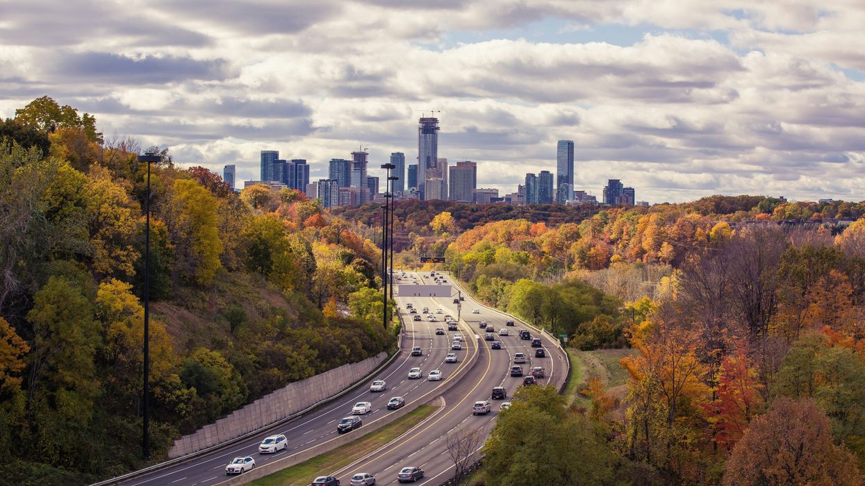 highway in toronto surrounded by fall coloured trees and the city skyline in the background
