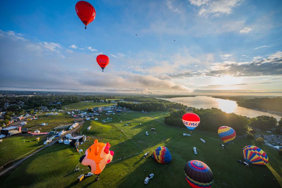 Hot air balloons flying over a festival at sunrise.