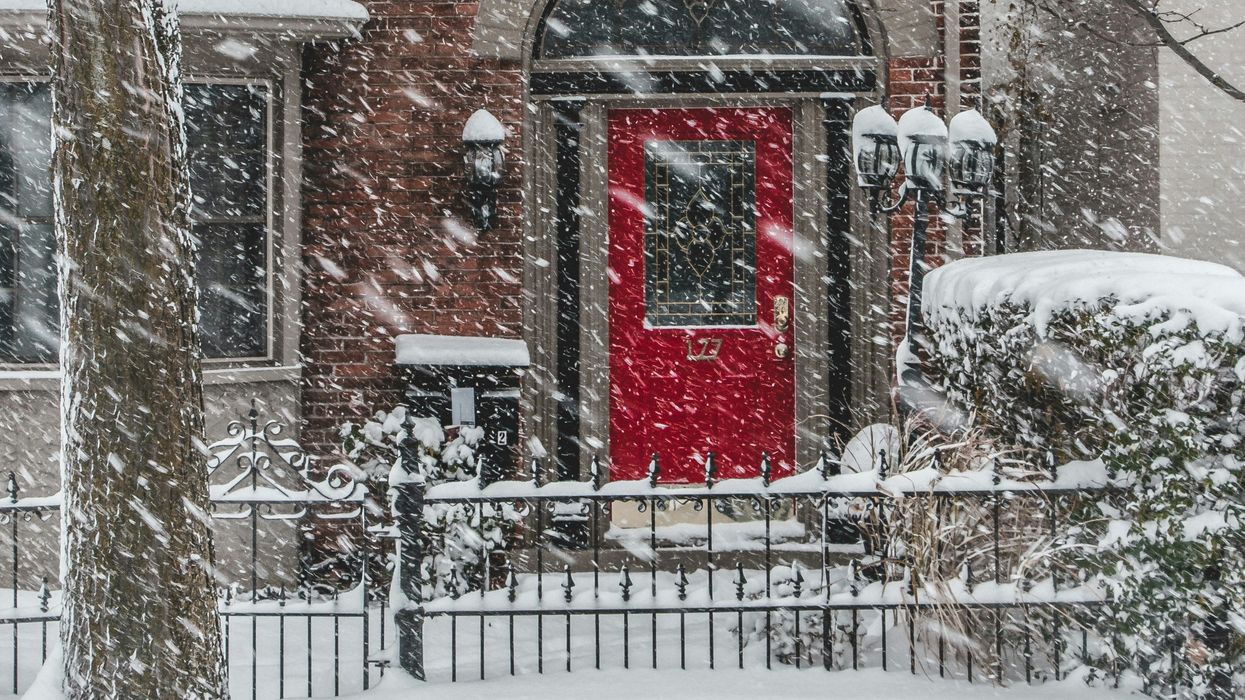 house with red door and black fence covered in snow during a snowstorm