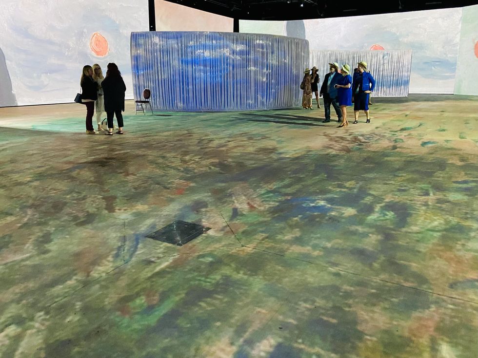 "Impression, soleil levant" painting displayed at Imagine Monet with guests wearing straw hats.