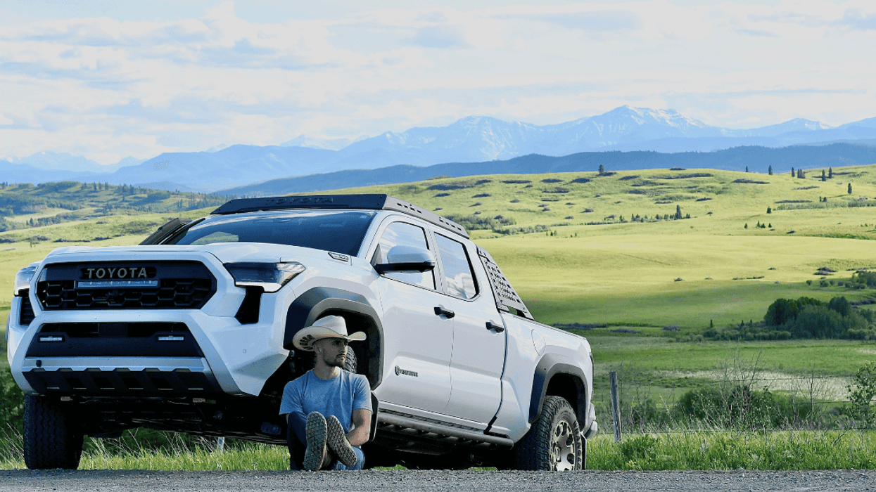 Jake Peacock wearing a cowboy hat leans against the tyre of his Toyota Tacoma truck with the Alberta prairies behind.