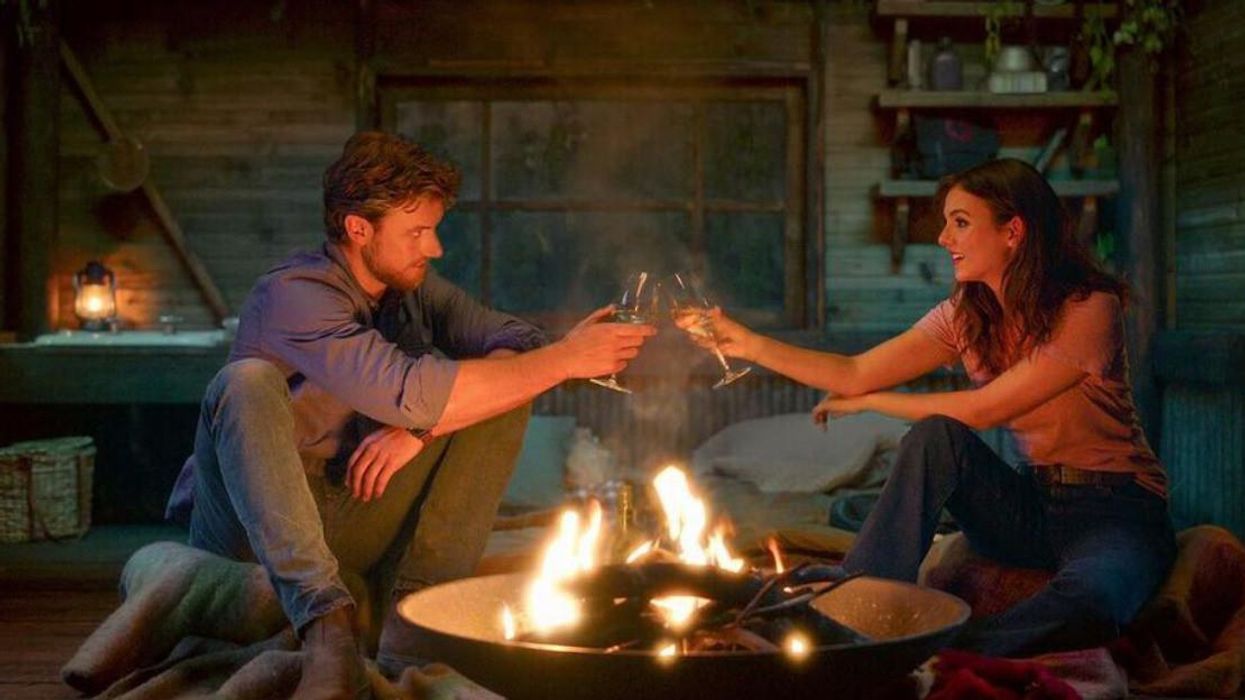 L'acteur et l'actrice principale du film A Perfect Pairing assis à côté d'un feu en cognant leur boisson.