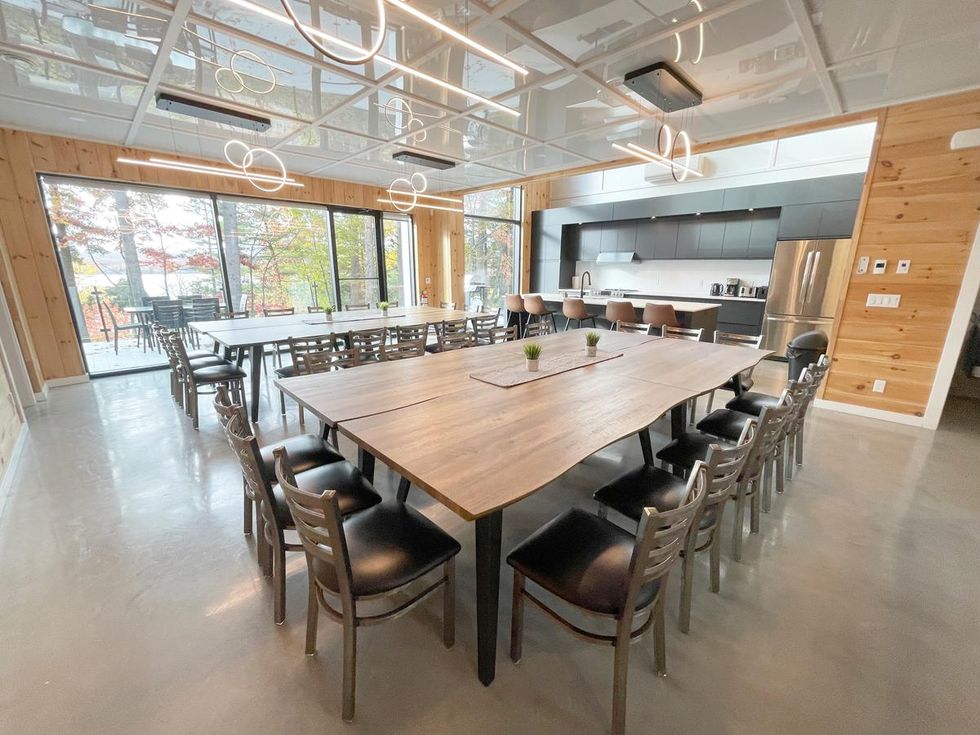 La cuisine du chalet avec deux grandes tables et une grande baie vitr\u00e9e donnant sur le lac.