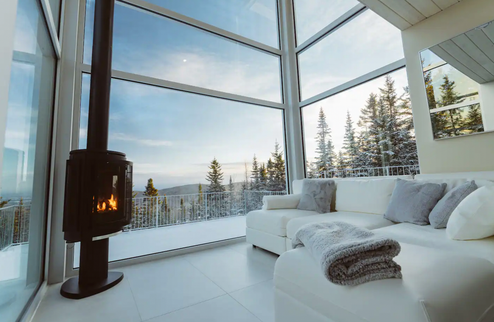 la vue sur les montagne, le foyer allum\u00e9 et le divan blanc du salon d'un airbnb \u00e0 louer