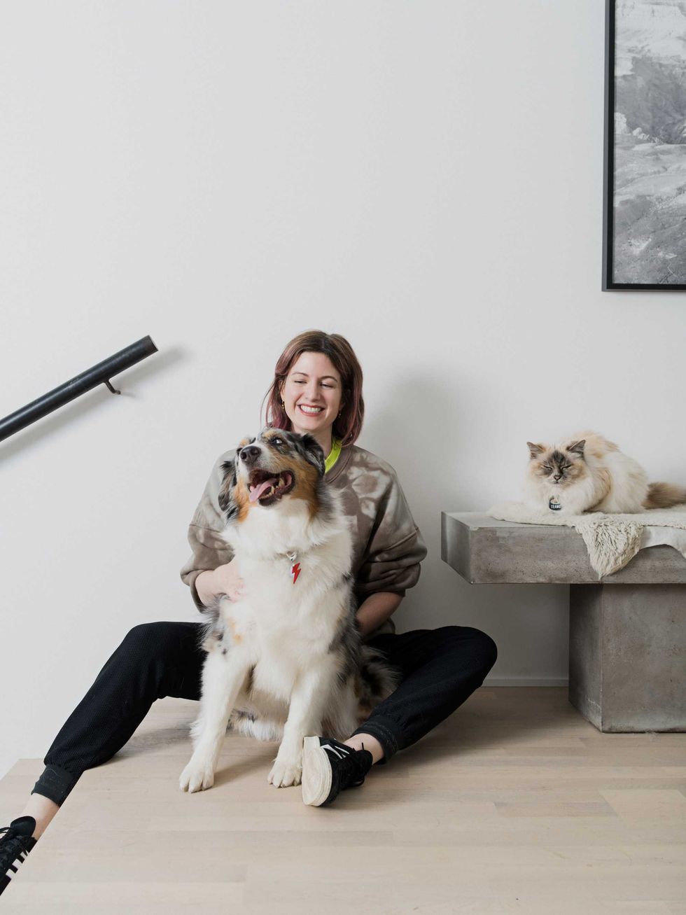 Laurel Murray sitting on the floor with an Australian shepherd dog and a cat snoozing on a stone bench next to her