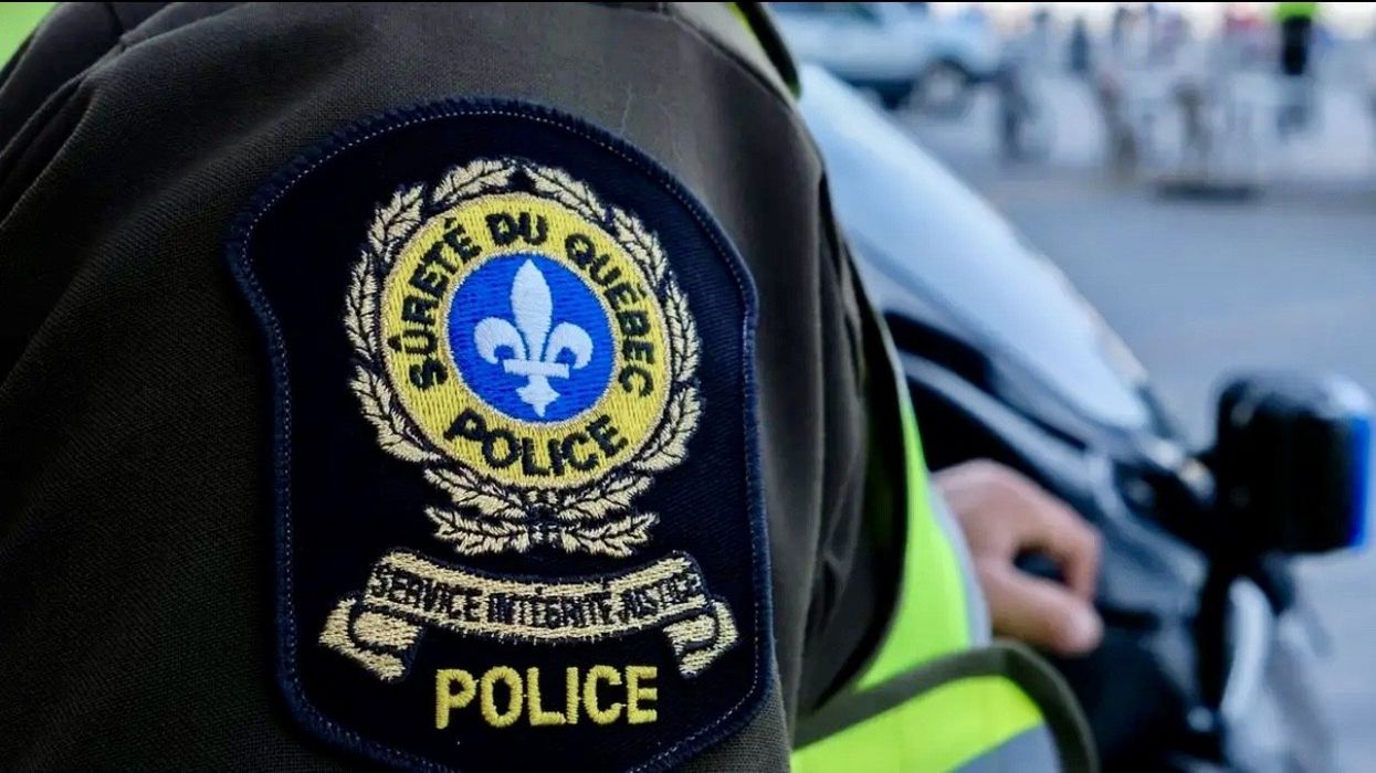 Le logo de la Sûreté du Québec (SQ) sur la manche d'un uniforme de travail d'une personne devant un véhicule.