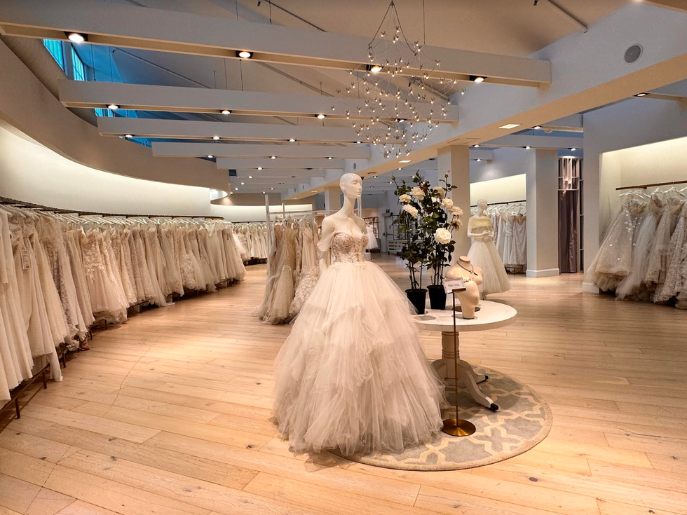 Light wooden floor with racks of white bridal gowns and mannequins in bridal gowns.