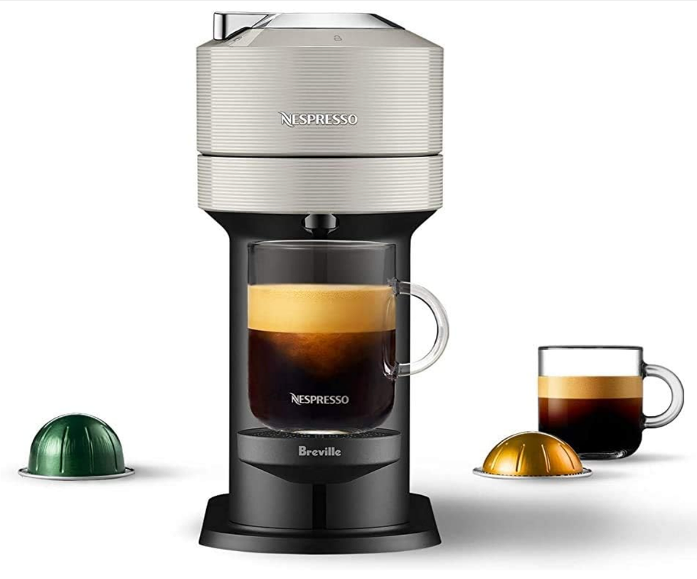Machine \u00e0 caf\u00e9 Nespresso noire et gris p\u00e2le, avec deux tasses de caf\u00e9 et des capsules.