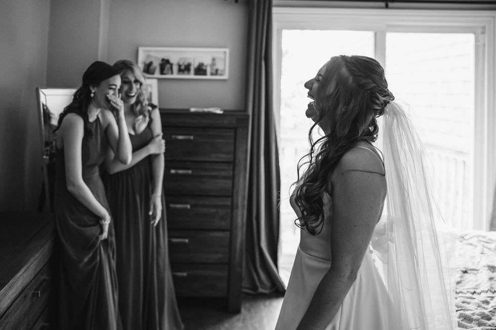 Maids of honour laughing with the bride as they help her get ready for the wedding.