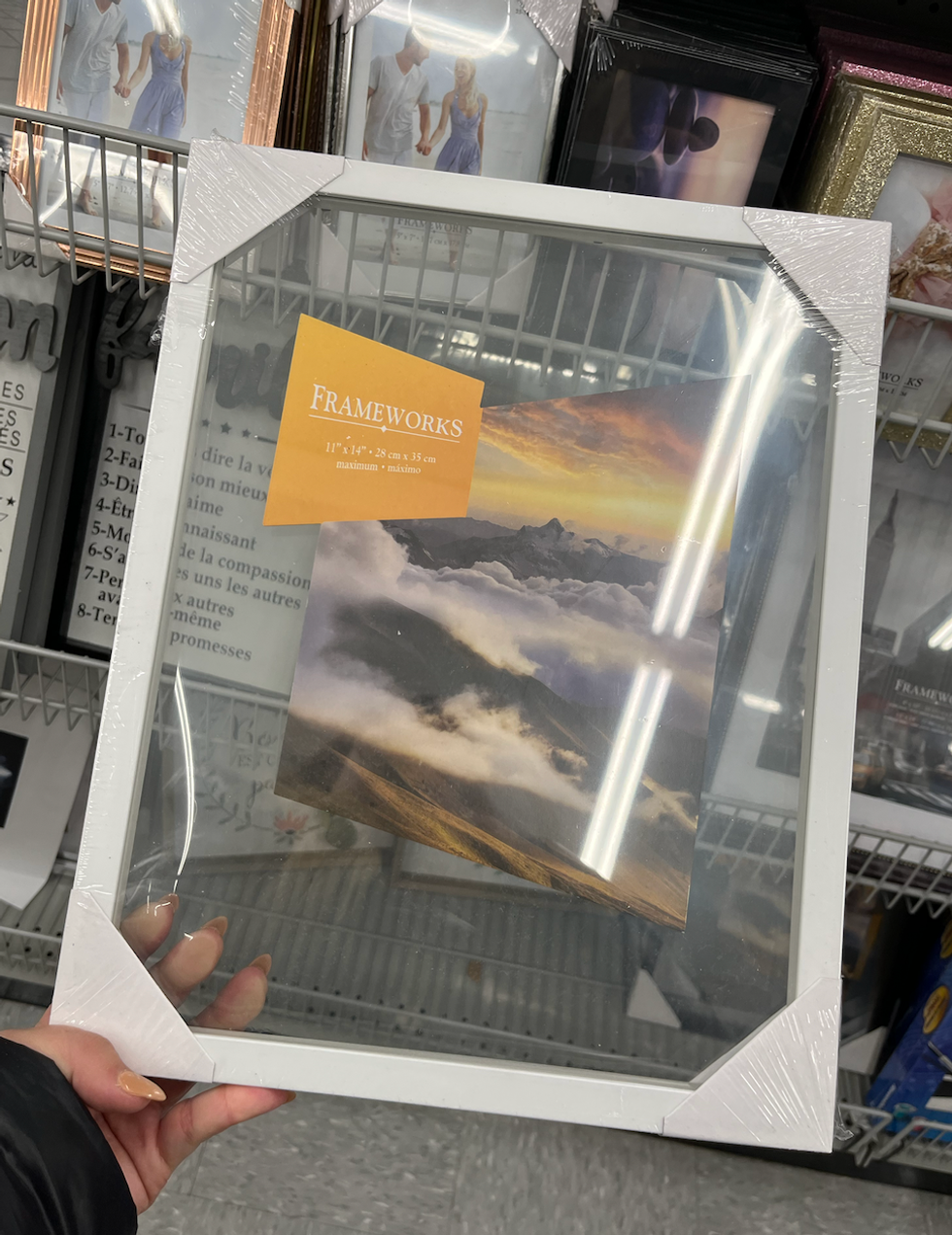 Main qui tient un cadre transparent avec bordure blanche du Dollarama.