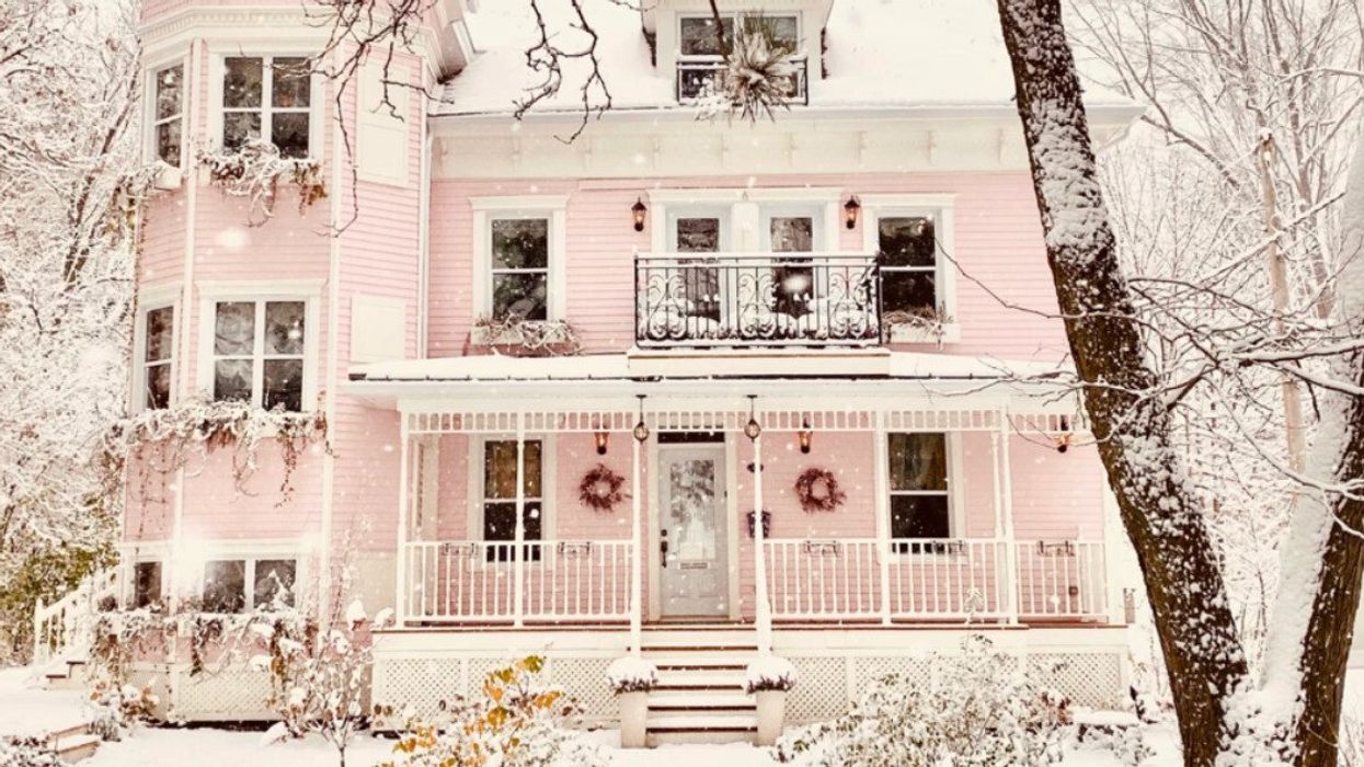 Maison rose entourée d'arbres et recouverte de neige.