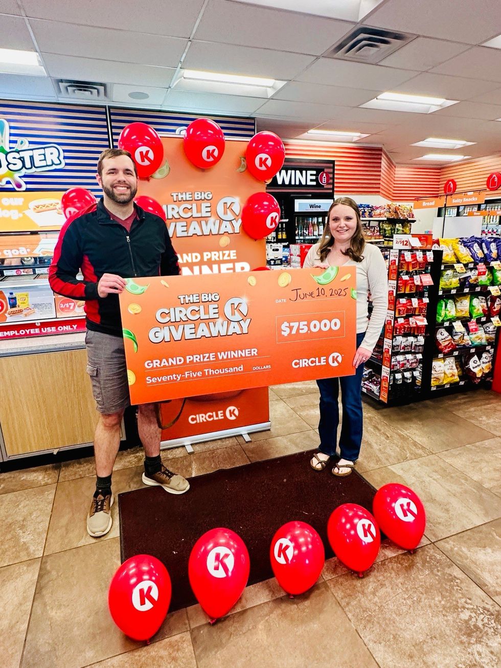 Man and woman holding a large Circle K Giveaway cheque for $75,000 inside a Circle K convenience store, with celebratory red balloons and branded displays.