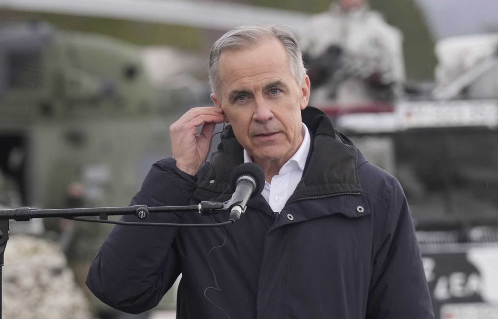 Mark Carney adjusts an earpiece standing outside by a microphone.