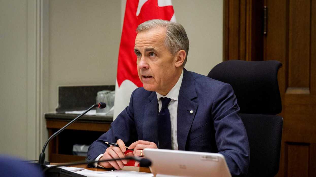 Mark Carney sits at a table and speaks into a microphone.