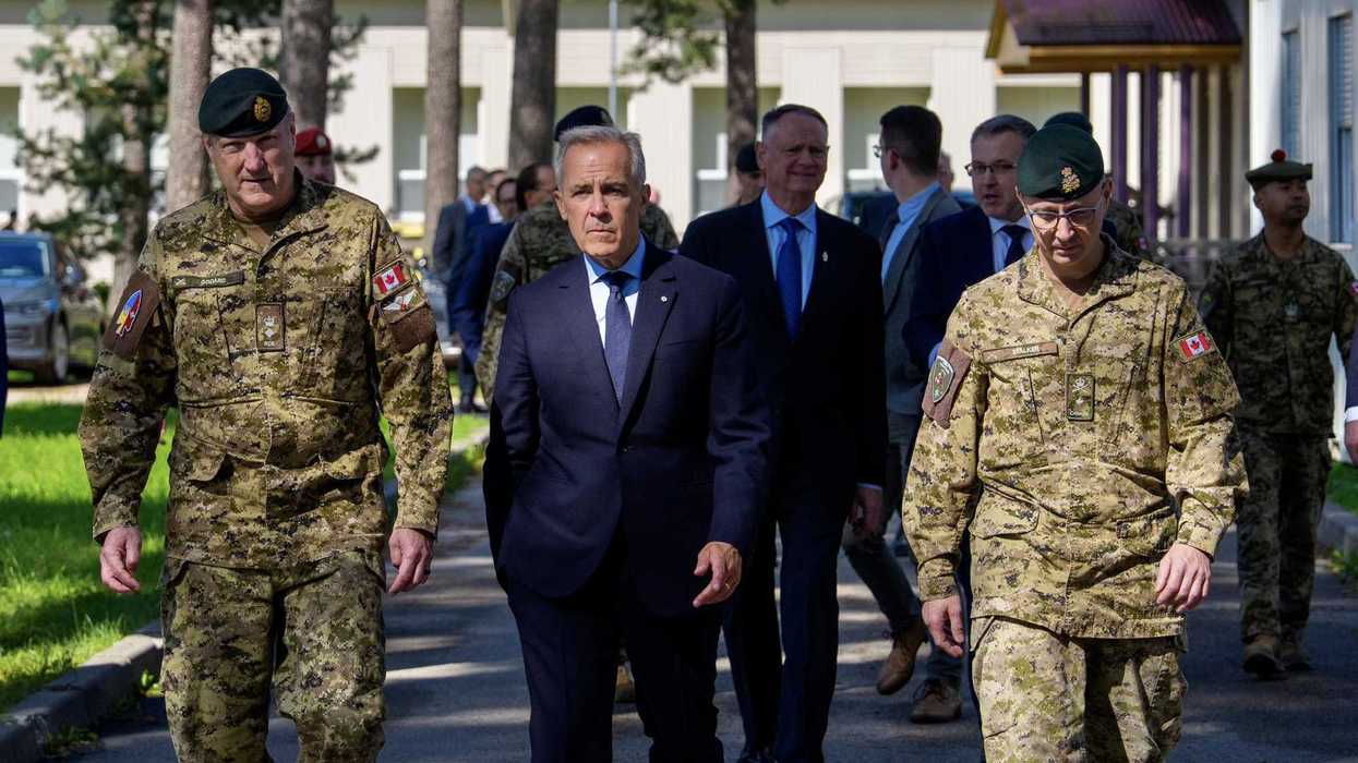 Mark Carney walks with two Canadian soldiers.