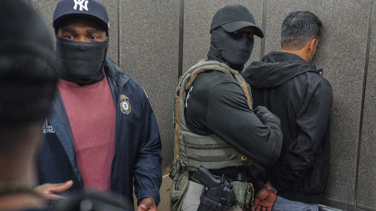 Masked ICE agents push a handcuffed detainee face-first against an elevator wall.