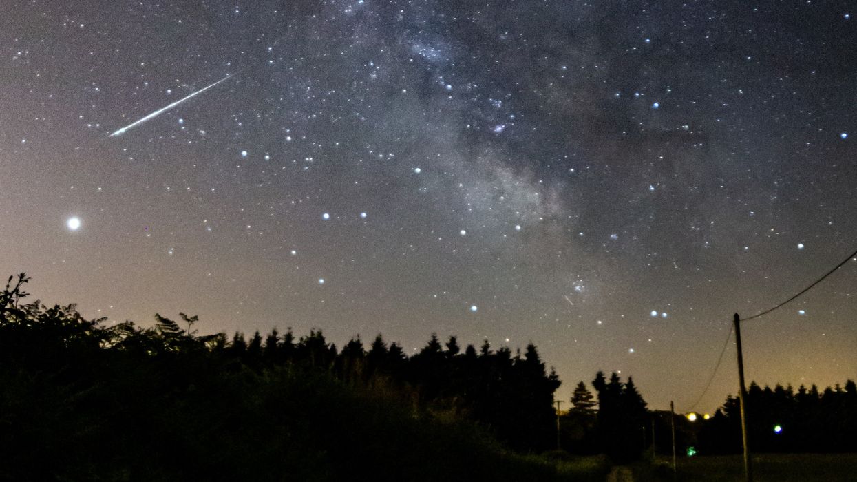 Meteor streaking across the sky above a road and trees.
