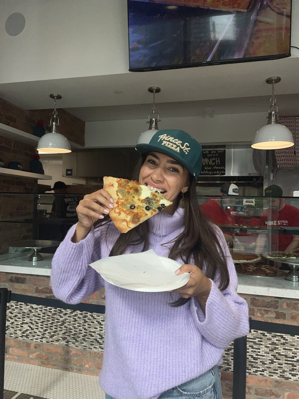 Mira wearing Prince St. Pizza merch and eating a pie.