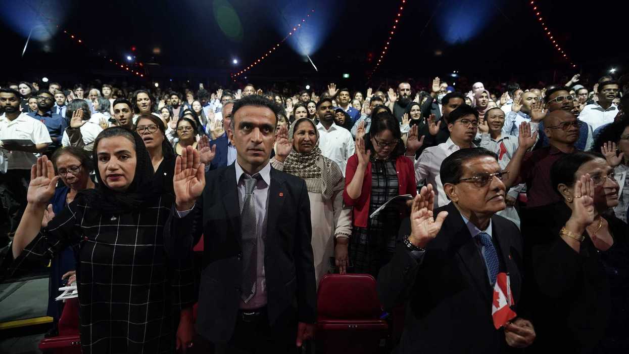 New Canadians stand with their right hand in the air as they take an oath of citizenship.