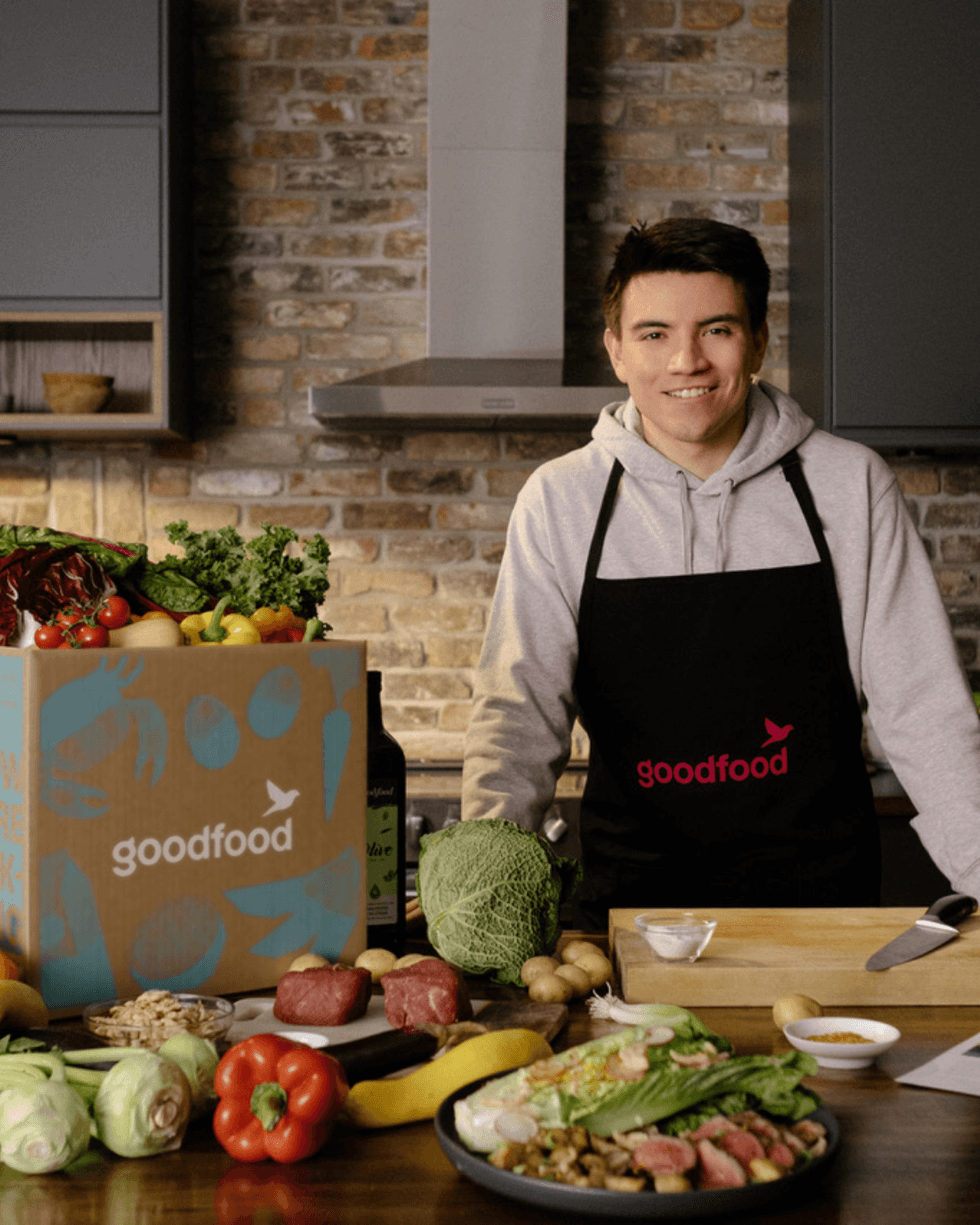 Nick Suzuki poses with fresh ingredients arranged on a counter and a Goodfood box.
