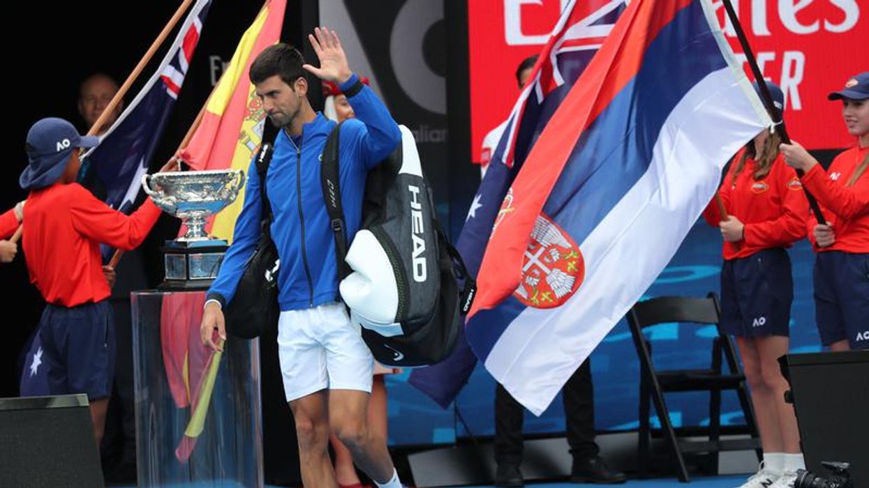 Novak Djokovic holds up a hand to wave while on the court.
