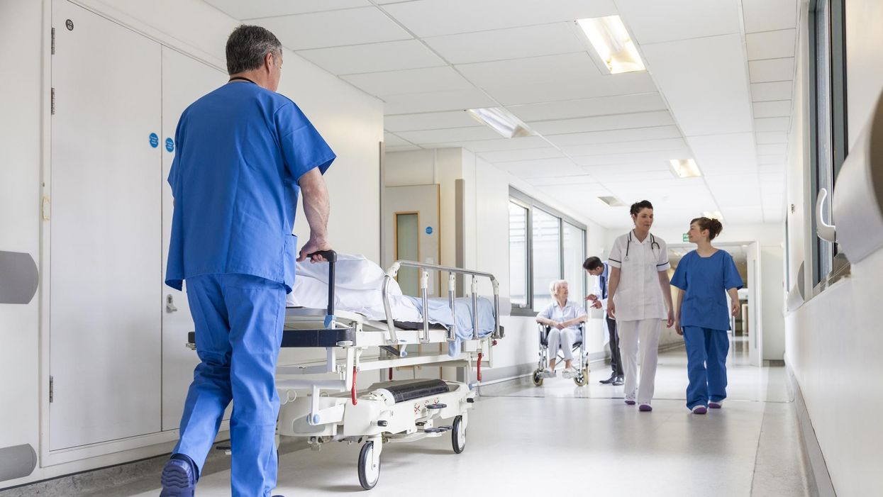 Nurse pushing a bed in a hospital corridor with doctors and senior female patient.
