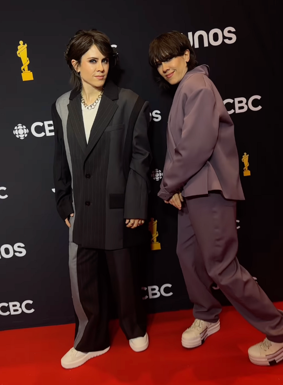One person wearing a black suit with white sneakers and another wearing a purple suit and white sneakers.