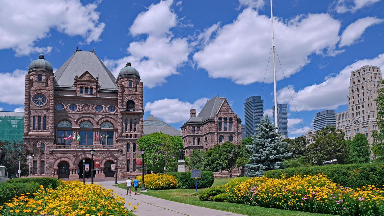 Ontario legislature buildings behind a sidewalk and flower bushes.