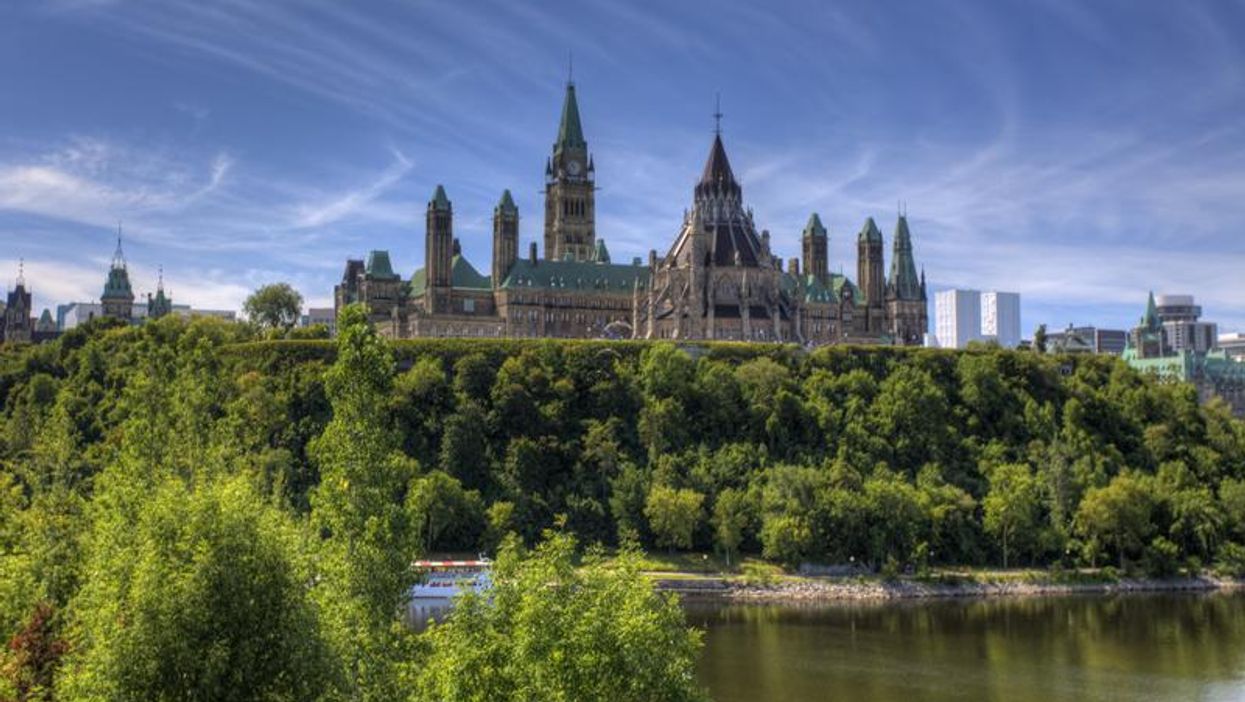 Ottawa's sunny skyline over the Parliament building, leafy trees, and a body of water.