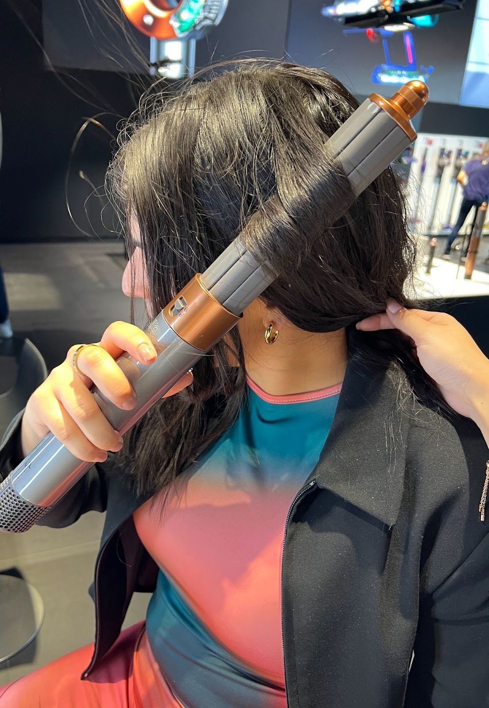 Paige McPhee using a copper and grey Dyson Airwrap to curl a section of her hair.