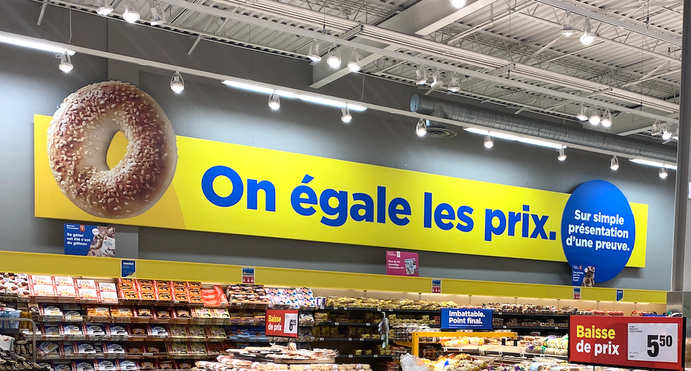 Pancarte jaune et bleue dans un Maxi indiquant \u00ab On \u00e9gale les prix. Sur simple pr\u00e9sentation d'une preuve. \u00bb avec l'image d'un bagel.