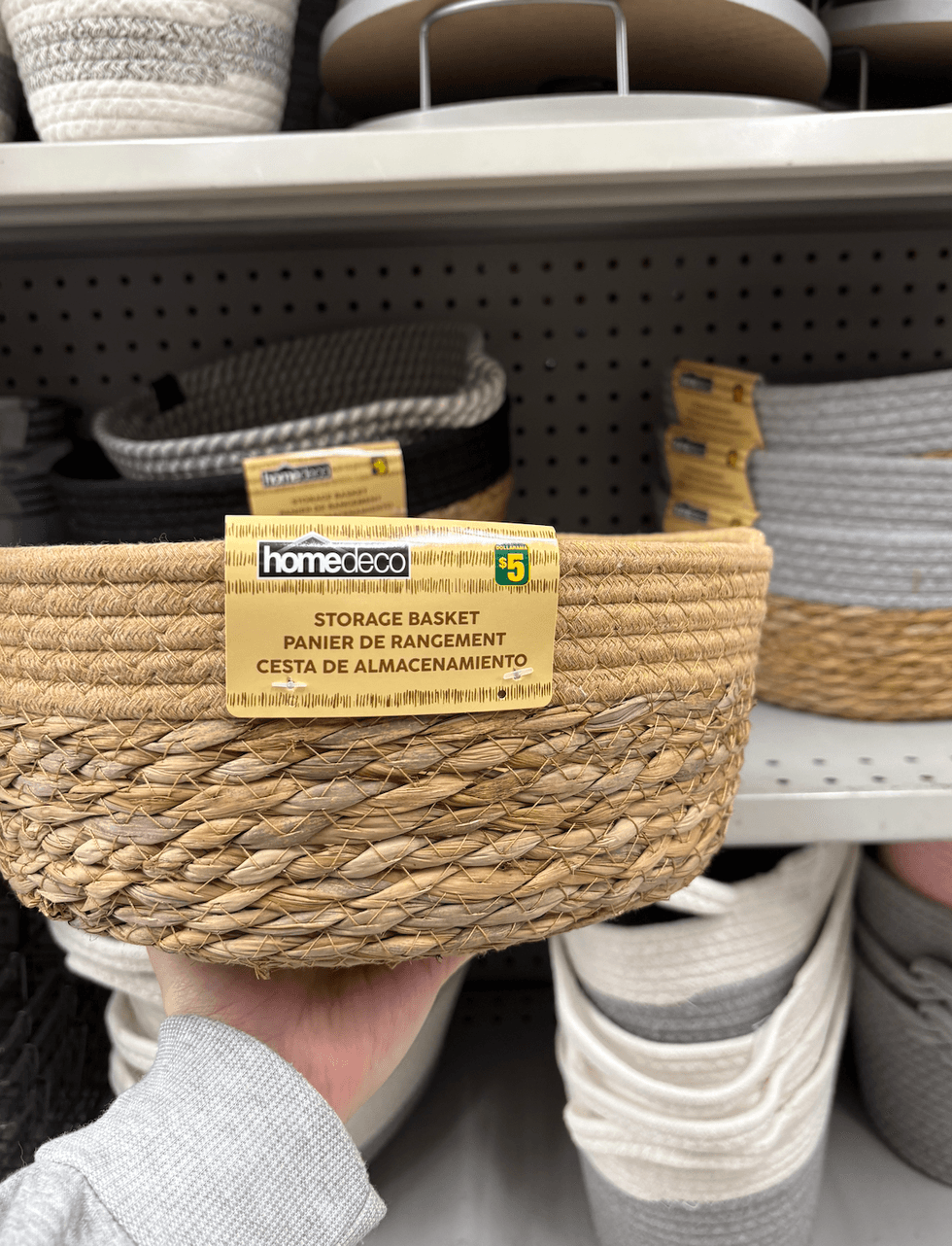 Paniers de rangement tenu par une main devant les tablettes du Dollarama.