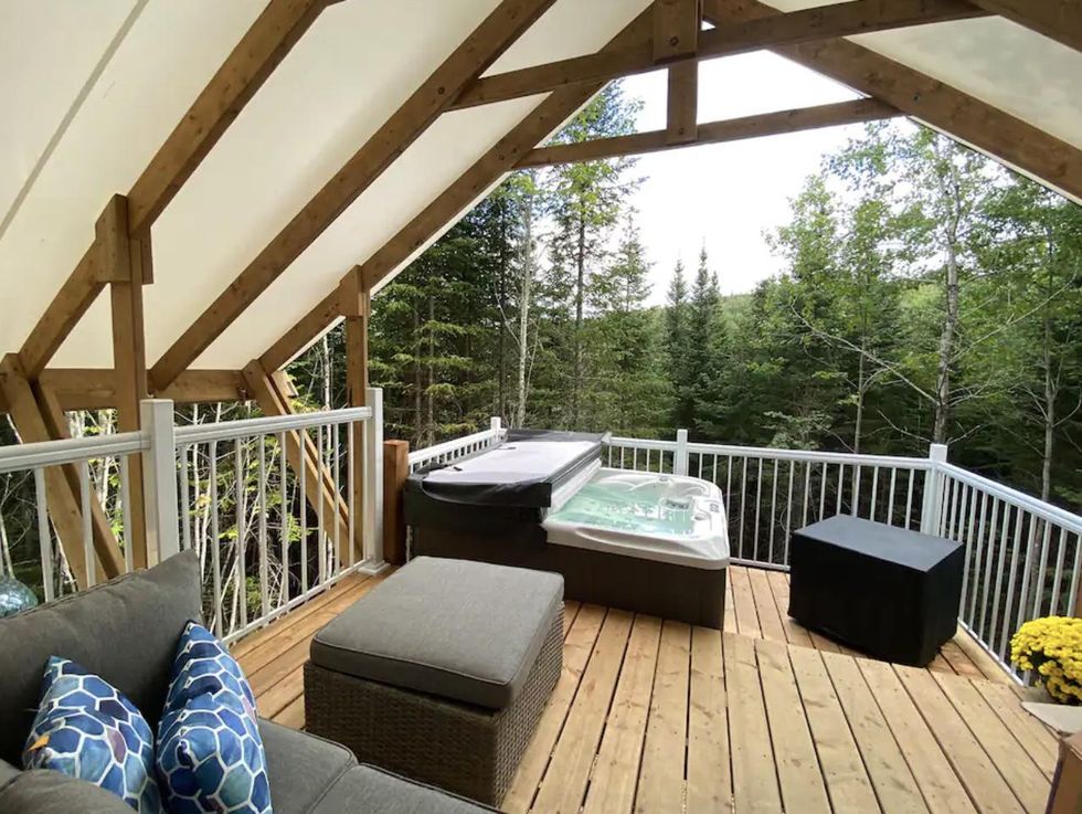 Patio en bois avec spa et si\u00e8ges, et vue sur la for\u00eat.