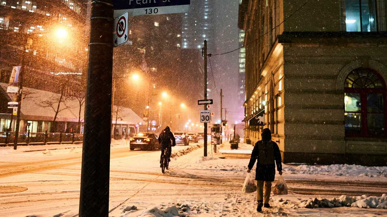 pedestrian, cyclist and cars along toronto street during snowstorm at night