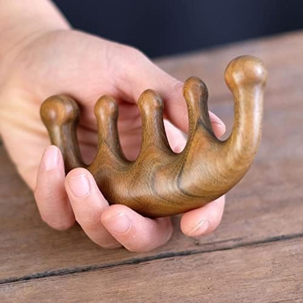 Peigne de massage en bois pour le cuire chevelu pr\u00e9sent\u00e9 dans une main.