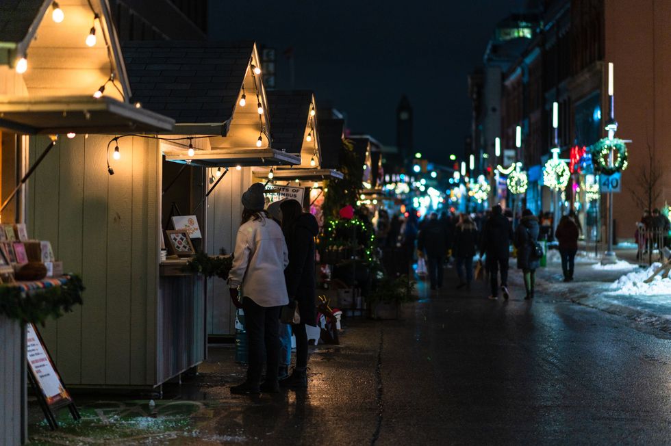 People are seen standing at glowing wooden kiosks at Christkindl in Kitchener.