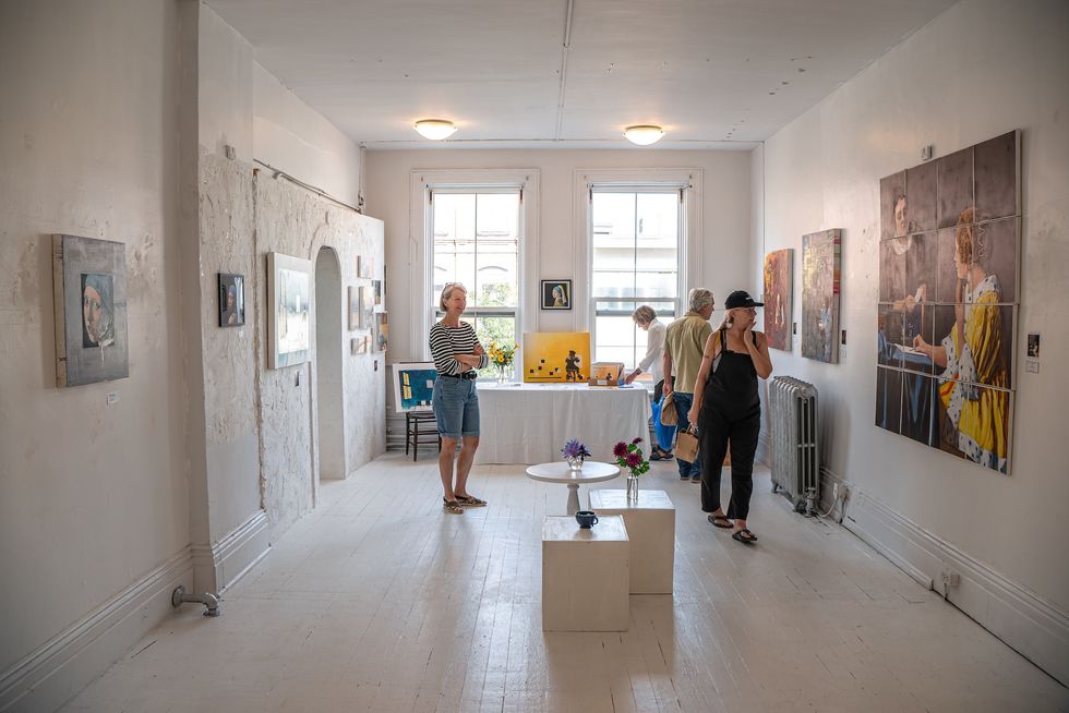 People browse a brightly lit art gallery in a historic building. 