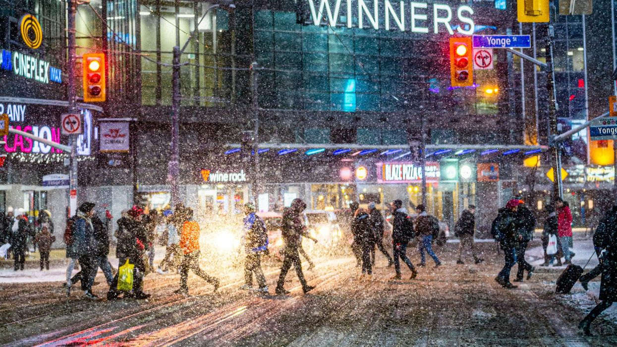 people crossing a downtown toronto street in the dark during a snowstorm