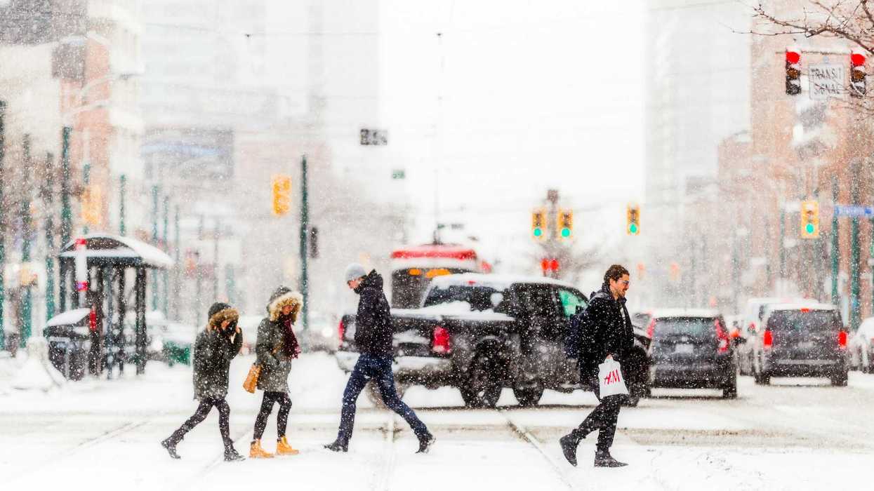 people crossing toronto street in front of cars and streetcar while it snows
