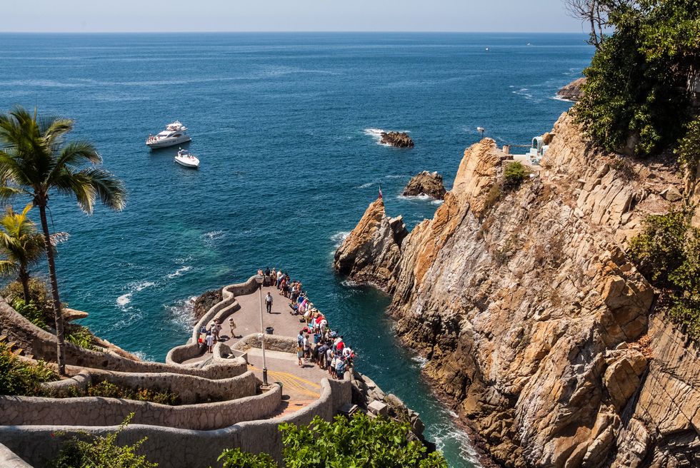 People gather at a cliff on the water in Mexico.