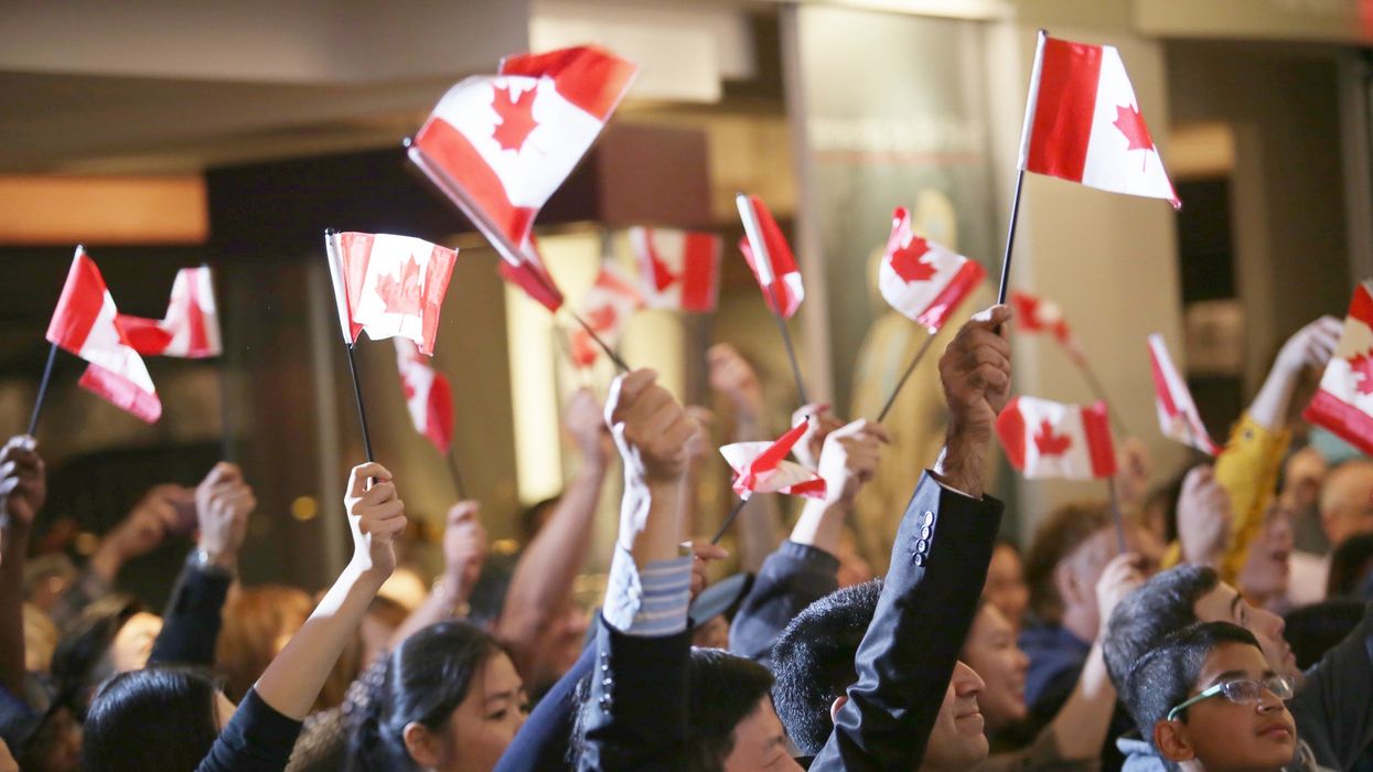 People holding Canadian flags during a citizenship ceremony.