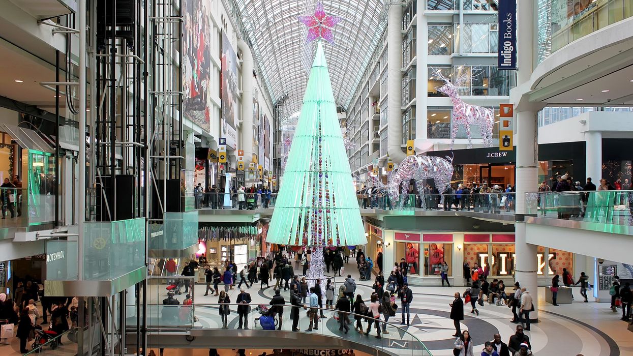 people in a mall in toronto that has a lit up green christmas tree and white and pink reindeer