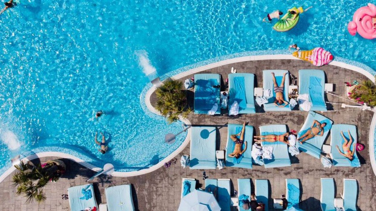 People on sun loungers by a swimming pool.